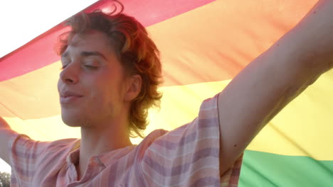 Porträt-Eines-Glücklichen-Kaukasischen-Mannes-Mit-Regenbogen-LGBT-Flagge-Auf-Dem-Balkon-Zu-Hause,-Zeitlupe