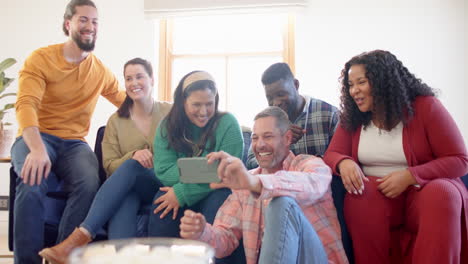 Happy-diverse-male-and-female-friends-relaxing-at-home-together-talking-and-looking-at-smartphone