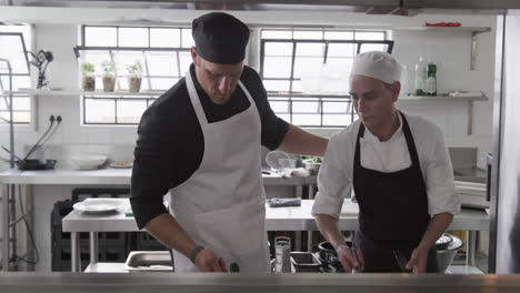 Focused-caucasian-male-chef-instructing-trainee-male-chefs-in-kitchen,-slow-motion