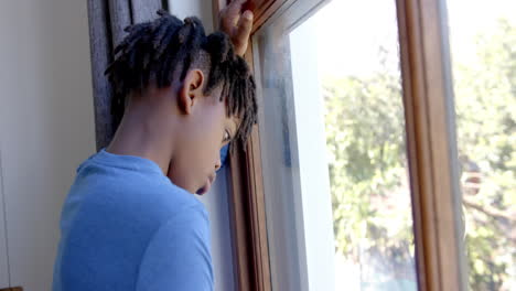 Thoughtful-african-american-boy-looking-through-window-at-home,-slow-motion