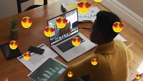 Animation-of-heart-eyes-face-emojis-over-african-american-woman-having-video-call-on-laptop