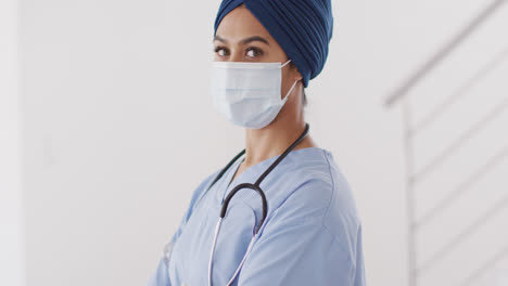 Video-of-biracial-female-doctor-in-hijab-and-face-mask-looking-at-camera