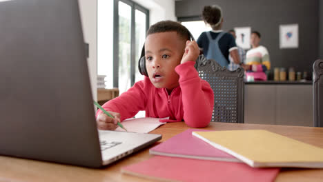African-american-boy-using-headphones-and-laptop-raising-hand-in-online-lesson,-slow-motion