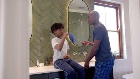 African-american-father-and-son-brushing-teeth-in-bathroom-at-home,-slow-motion