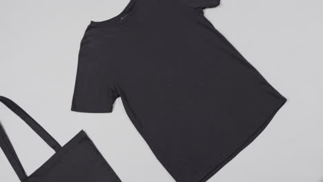 Nahaufnahme-Einer-Schwarzen-Tasche-Und-Eines-T-Shirts-Auf-Weißem-Hintergrund,-Mit-Kopierraum,-Zeitlupe