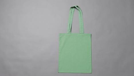 Close-up-of-green-bag-on-grey-background,-with-copy-space,-slow-motion
