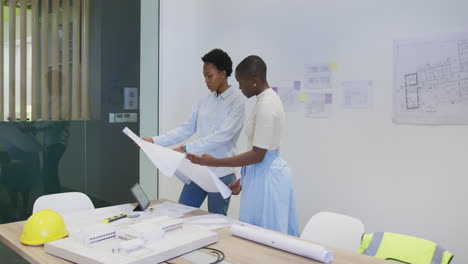 Two-african-american-female-architects-in-discussion-studying-blueprints-in-office