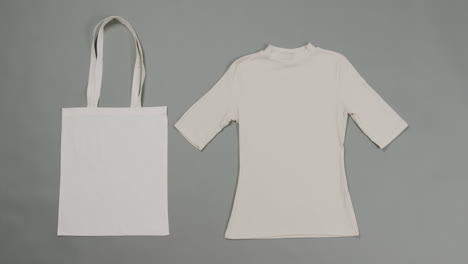 Close-up-of-white-bag-and-t-shirt-on-grey-background,-with-copy-space,-slow-motion