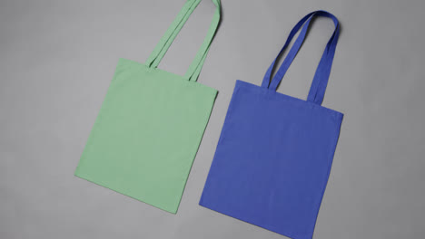 Close-up-of-green-and-blue-bags-on-grey-background,-with-copy-space,-slow-motion