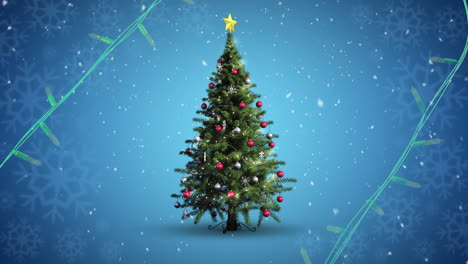 Yellow-string-lights-flashing-over-decorated-christmas-tree-and-falling-snow-on-blue-background