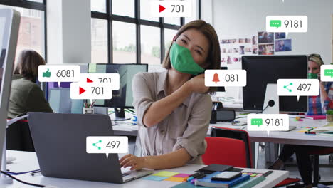 Animation-of-social-media-icons-over-portrait-of-asian-woman-removing-face-mask-smiling-at-office