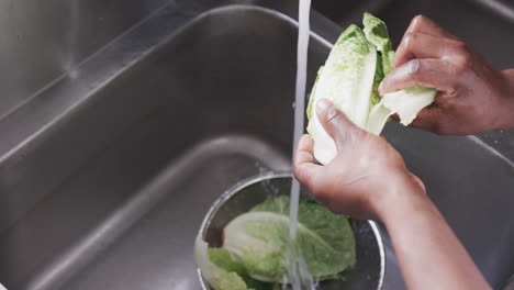 African-american-male-chef-washing-vegetables-in-sink-in-kitchen,-slow-motion