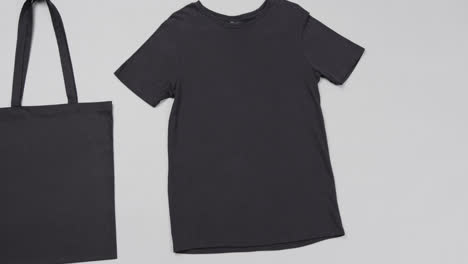 Primer-Plano-De-Bolsa-Negra-Y-Camiseta-Sobre-Fondo-Blanco,-Con-Espacio-Para-Copiar,-Cámara-Lenta