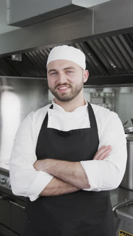Happy-caucasian-male-chef-standing-with-arms-crossed-in-kitchen,-slow-motion,-vertical
