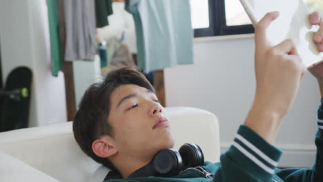 Asian-boy-playing-games-on-digital-tablet-lying-on-the-couch-at-home