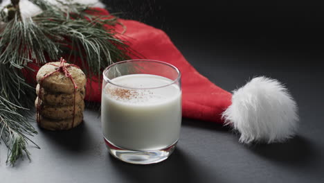 Video-of-christma-cookies,-glass-of-miljk,-santa-clasus-hat-and-copy-space-on-black-background