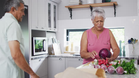 Feliz-Pareja-Birracial-Senior-Sosteniendo-Verduras-En-La-Cocina