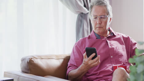 Senior-caucasian-man-sitting-on-sofa-and-using-smartphone,-slow-motion