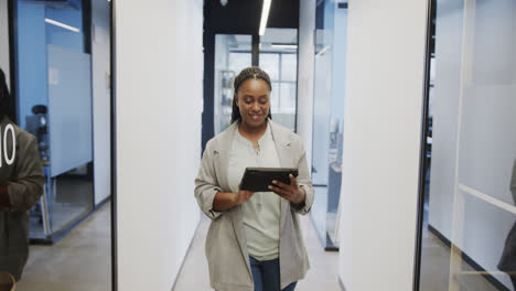 Happy-african-american-casual-businesswoman-using-tablet-walking-in-office-corridor,-slow-motion
