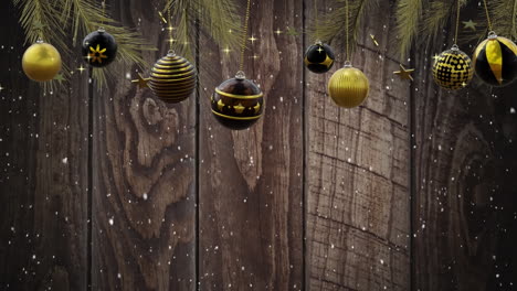 Swinging-black-and-gold-christmas-baubles-over-falling-snow-on-dark-wood-background