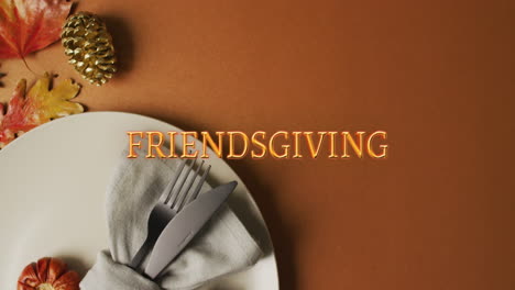 Animation-of-friendsgiving-text-over-cutlery-and-autumn-leaves-over-brown-background