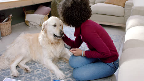 Happy-biracial-woman-petting-golden-retriever-dog-and-using-smartphone-at-home,-slow-motion