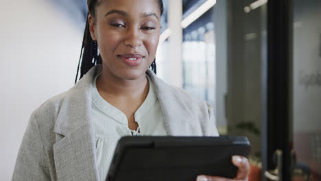 Portrait-of-happy-african-american-casual-businesswoman-using-tablet-in-office-corridor,-slow-motion