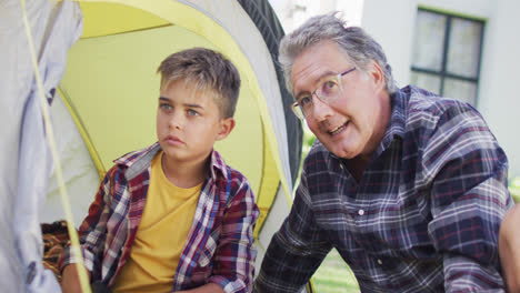Happy-caucasian-grandfather-and-grandson-sitting-in-tent-in-garden,-slow-motion