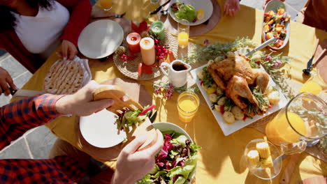 Happy-diverse-male-and-female-friends-serving-thanksgiving-celebration-meal-in-sunny-garden