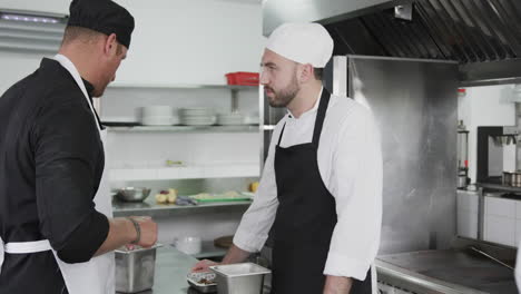 Focused-caucasian-male-chef-instructing-trainee-male-chef-in-kitchen,-slow-motion