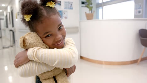 Portrait-of-happy-african-american-girl-hugging-mascot-in-hospital,-slow-motion