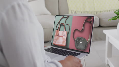 Biracial-woman-using-laptop-at-home-online-shopping-for-handbags,-slow-motion