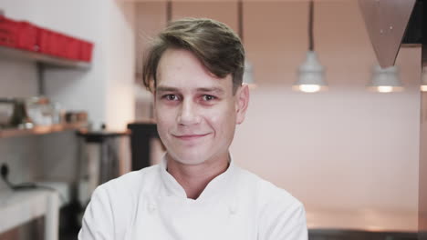 Portrait-of-happy-caucasian-male-chef-smiling-in-restaurant-kitchen,-slow-motion