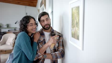 Happy-biracial-couple-looking-at-painting-on-wall-at-home,-in-slow-motion
