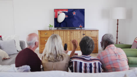 Diverse-senior-friends-watching-tv-with-rugby-ball-on-flag-of-new-zealand-on-screen