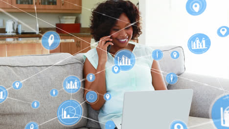 Animation-of-connected-icons-over-african-american-woman-talking-on-cellphone-and-working-on-laptop