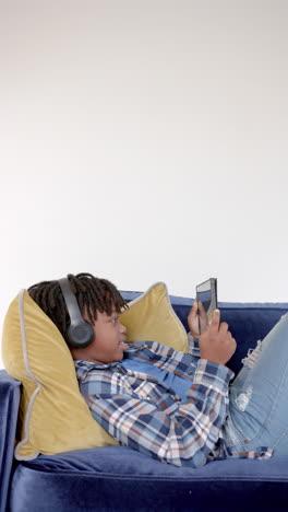 Vertikales-Video-Eines-Afroamerikanischen-Jungen,-Der-Zu-Hause-Mit-Einem-Smartphone-Auf-Dem-Sofa-Liegt,-Zeitlupe