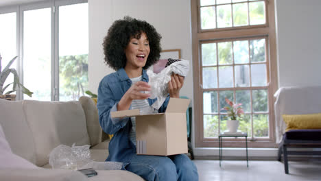 Happy-biracial-woman-unpacking-shopping-box-at-home,-slow-motion