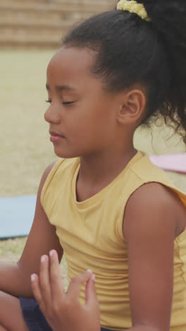 Video-of-focused-diverse-girls-practicing-yoga-on-mats-in-front-of-school