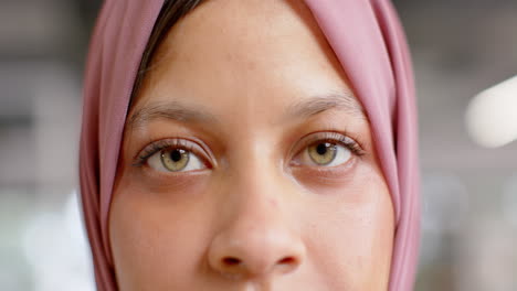 Portrait-of-happy-eyes-of-biracial-casual-businesswoman-in-hijab-in-office,-slow-motion