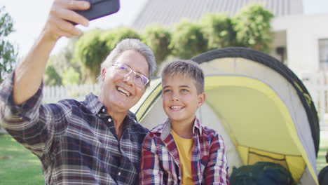 Glücklicher-Kaukasischer-Großvater-Und-Enkel-Sitzen-Im-Zelt-Und-Machen-Selfie,-Zeitlupe
