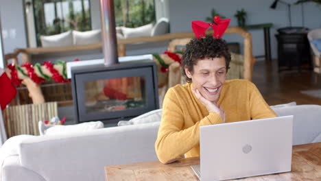 Happy-biracial-man-using-laptop-for-video-call-at-home-at-christmas,-slow-motion,-copy-space