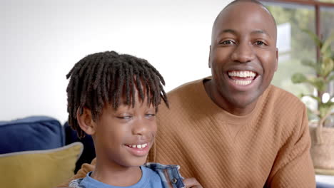 Portrait-of-happy-african-american-father-and-son-embracing-on-sofa-at-home,-slow-motion