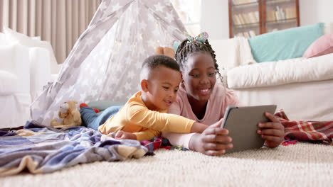 Happy-african-american-sister-and-brother-using-tablet-and-smiling-at-home,-slow-motion