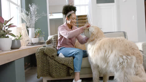 Happy-biracial-woman-petting-golden-retriever-dog-at-home,-slow-motion