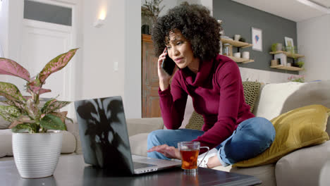 Mujer-Birracial-Feliz-Usando-Una-Computadora-Portátil-Y-Hablando-Por-Teléfono-Inteligente-En-Casa,-Cámara-Lenta