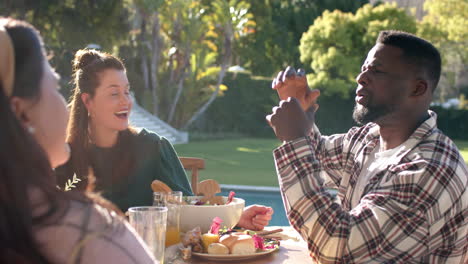 Happy-diverse-male-and-female-friends-talking-during-thanksgiving-celebration-meal-in-sunny-garden