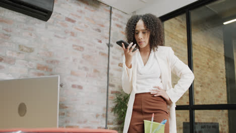 Vielbeschäftigte,-Gemischtrassige-Geschäftsfrau,-Die-Im-Büro-In-Zeitlupe-Auf-Dem-Smartphone-Spricht-Und-Den-Laptop-Benutzt