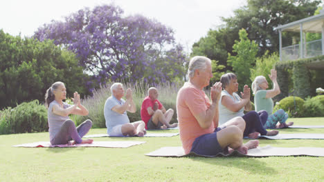 Diverse-group-of-male-and-female-seniors-practicing-yoga-meditation-in-sunny-garden,-slow-motion