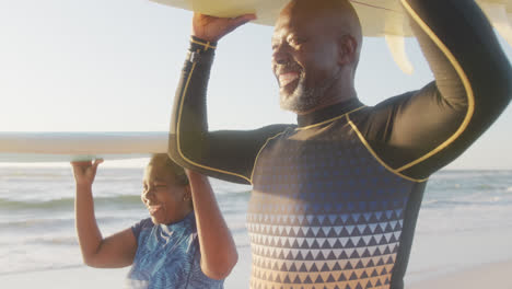 Glückliches-älteres-Afroamerikanisches-Paar,-Das-In-Zeitlupe-Am-Strand-Spazieren-Geht-Und-Surfbretter-Hält
